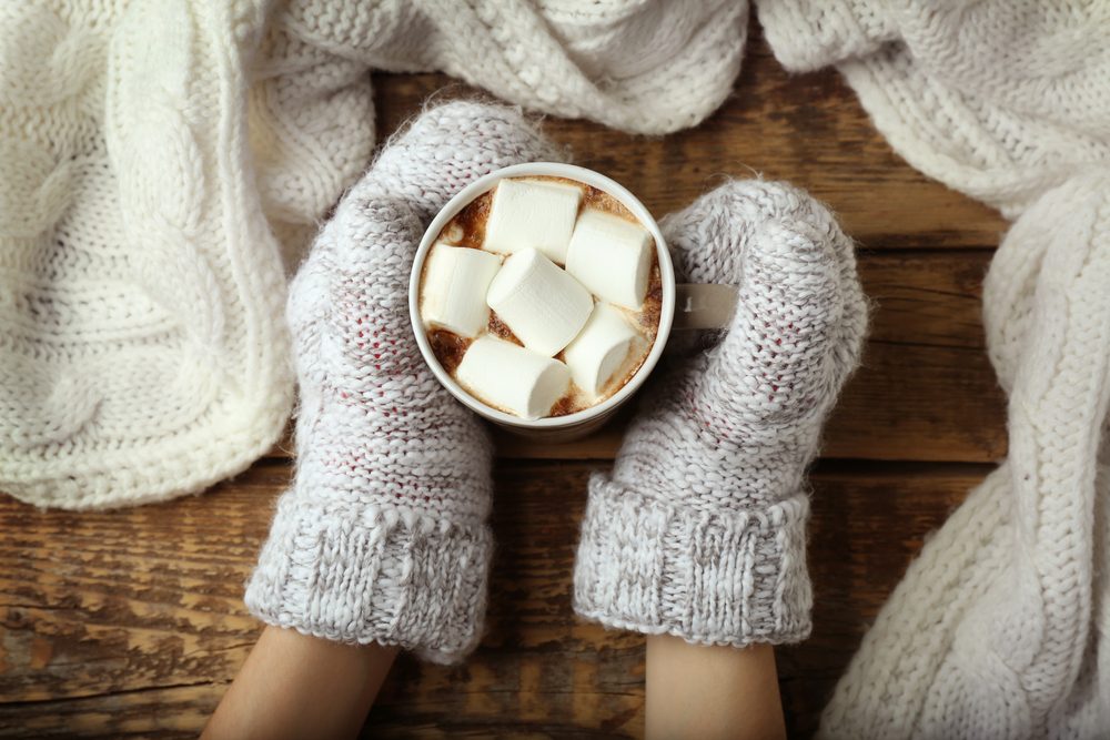 woman,holding,cup,of,hot,cocoa,with,marshmallows,on,table