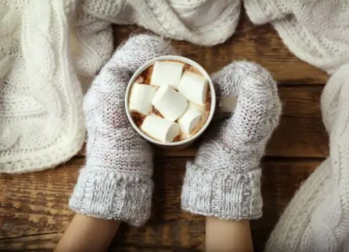 woman,holding,cup,of,hot,cocoa,with,marshmallows,on,table